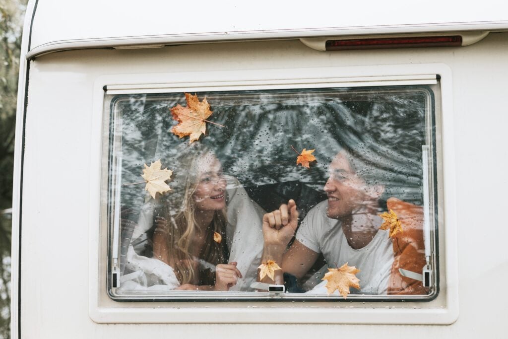 A couple sitting in the window of their RV watching the autumn leaves fall 