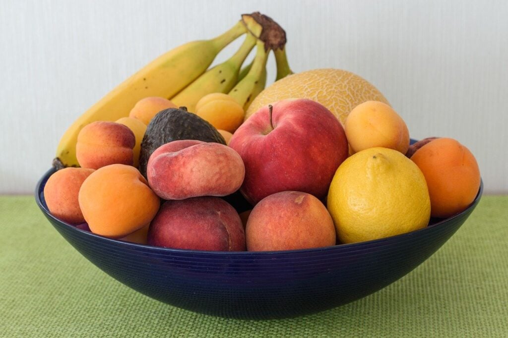 variety of fruit in a blue bowl on a green table cloth
