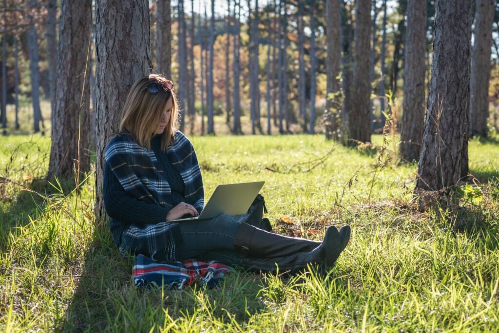 A woman sitting in the forest on her laptop using WiFi for RV living