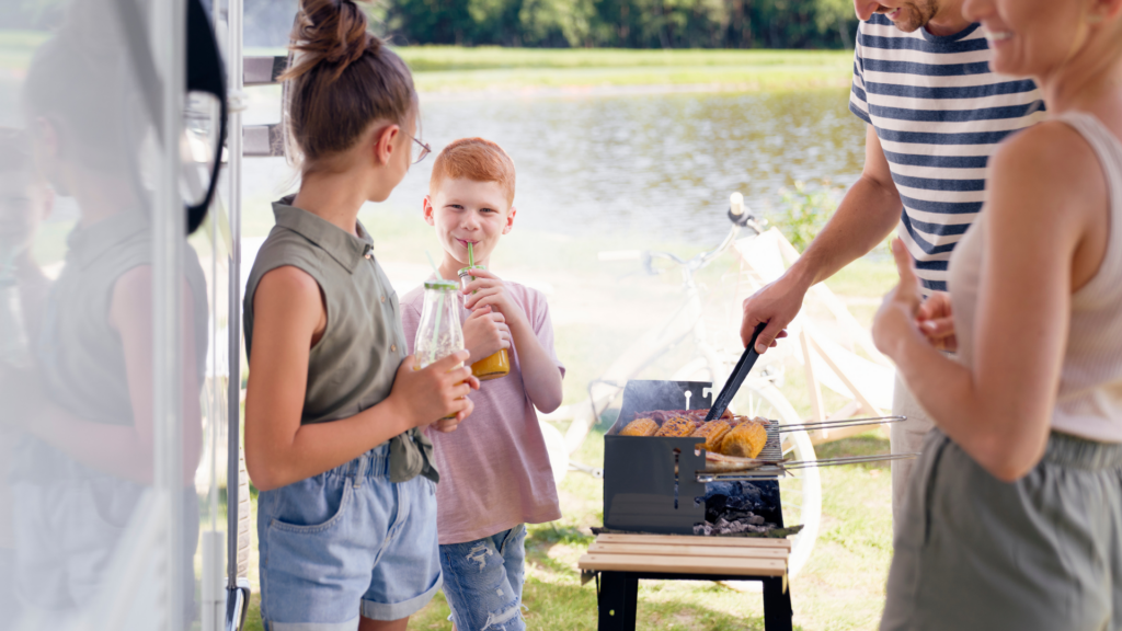 A mom and dad standing by the grill with two kids smiling at each other outside of an RV 