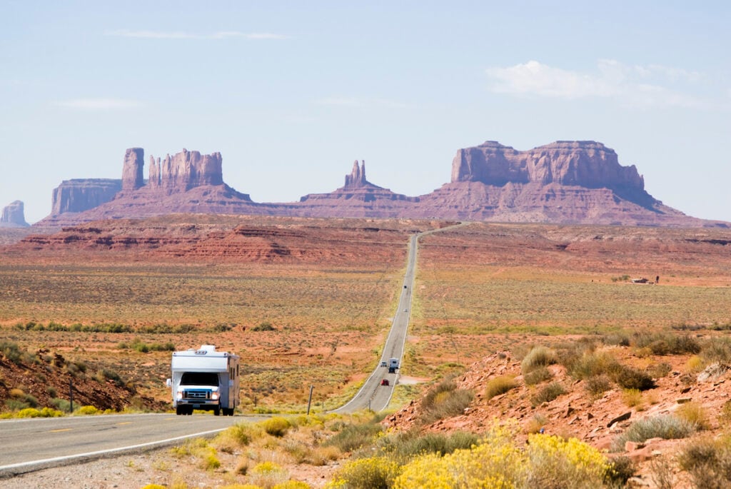 class c rv driving through monument valley on highway - cover photo for must haves for RV camping