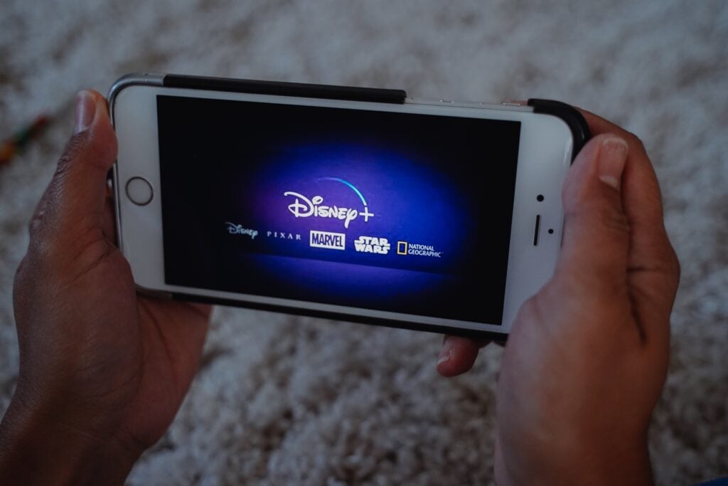 Two hands holding a cell phone with the Disney+ app loading. 