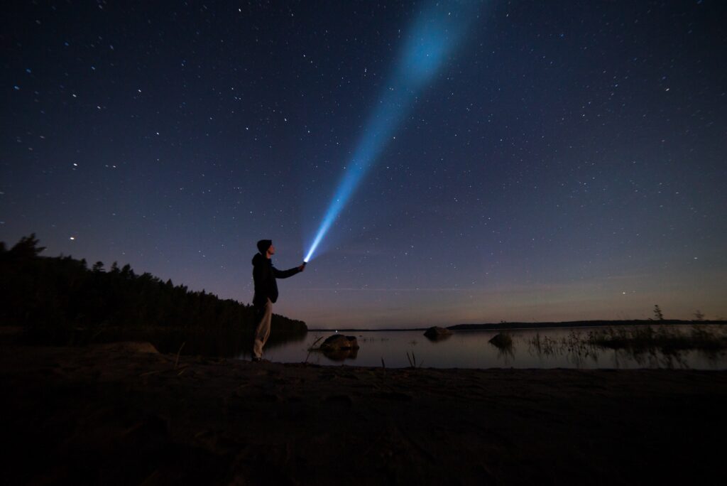 A man holding a flashlight shining it up at the sky at night 