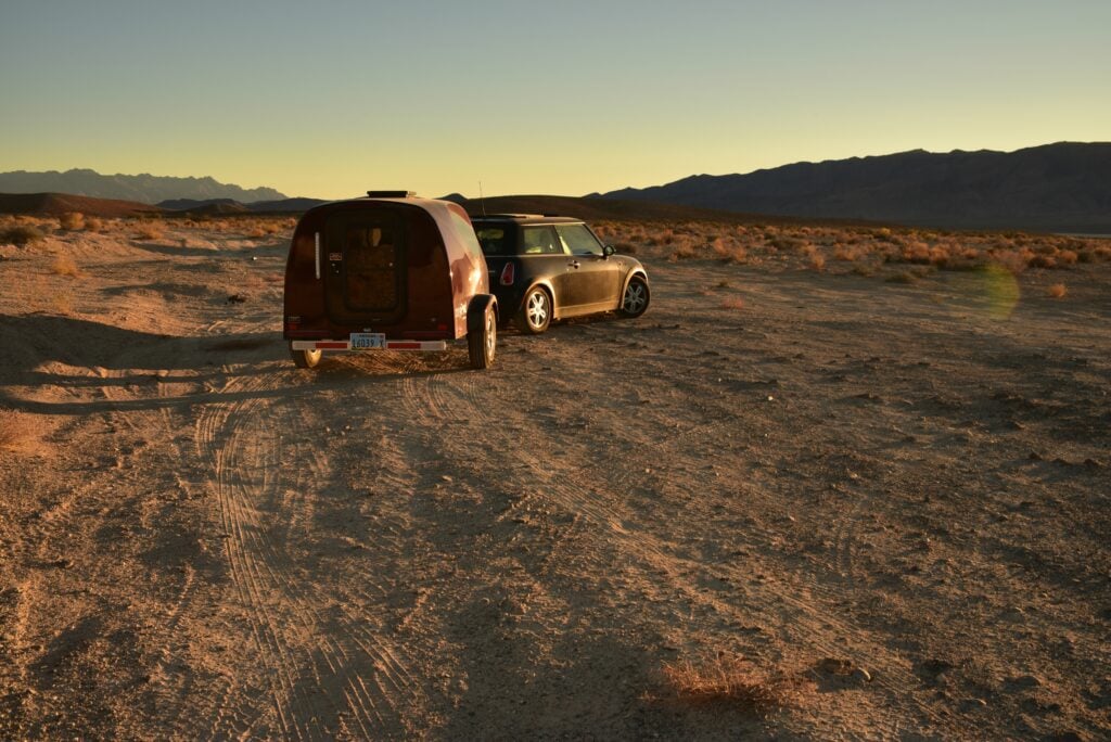 A mini cooper pulling a small travel trailer boondocking in the desert.
