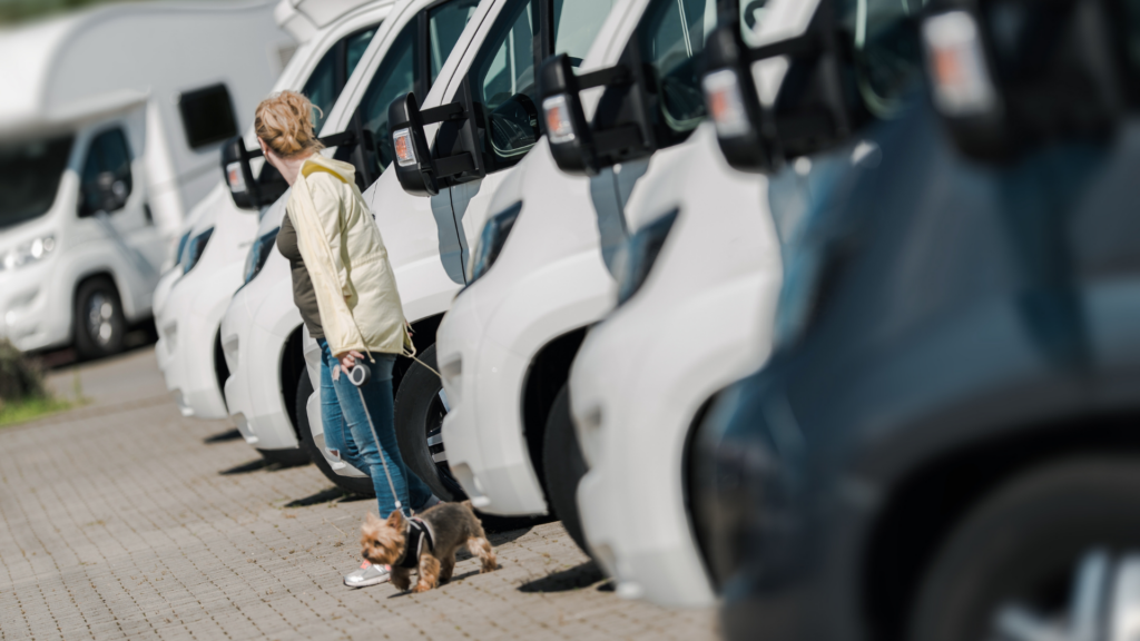 A woman with her dog on a leash looking at a row of RVs. She's considering buying an RV out of state. 