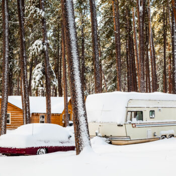 RV covered in snow near cabin in the woods - ways to keep snow off RV roof