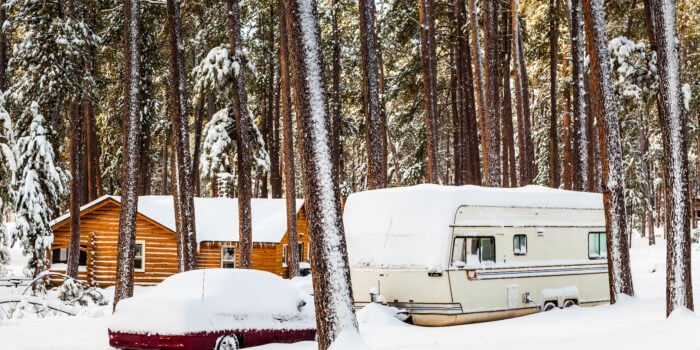 RV covered in snow near cabin in the woods - ways to keep snow off RV roof