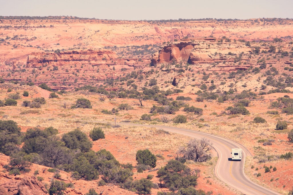 RV on road surrounded by landscape - feature image for full time RV essentials