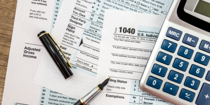 A 1040 tax form and other forms on a desk along with a pen and calculator