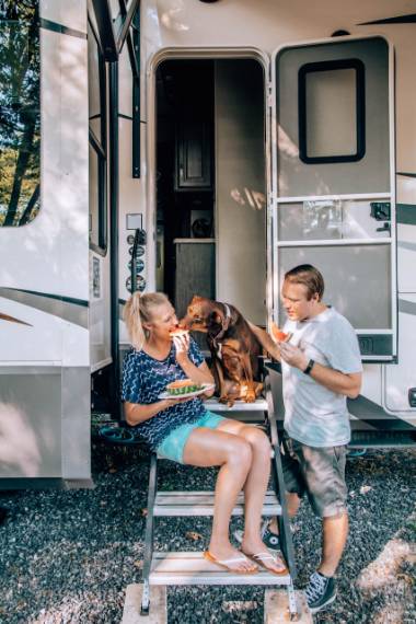 RVers Rae and Jason Miller sitting outside their RV door with their dog enjoying watermelon