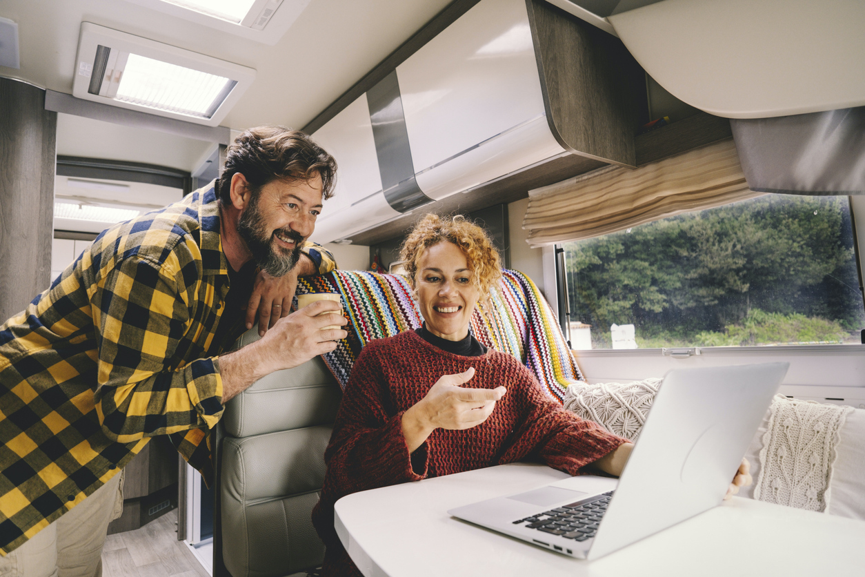 Adult couple enjoy work together using laptop computer sitting inside camper rv vehicle. Concept of nomad and alternative free job lifestyle. Modern man and woman people with technology (Adult couple enjoy work together using laptop computer sitting in RV