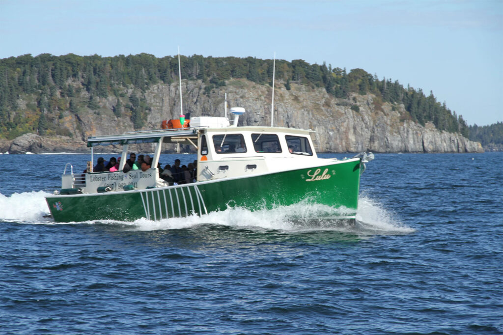 green boat on blue ocean with cliffs in background - things to do while camping in Bar Harbor, Maine
