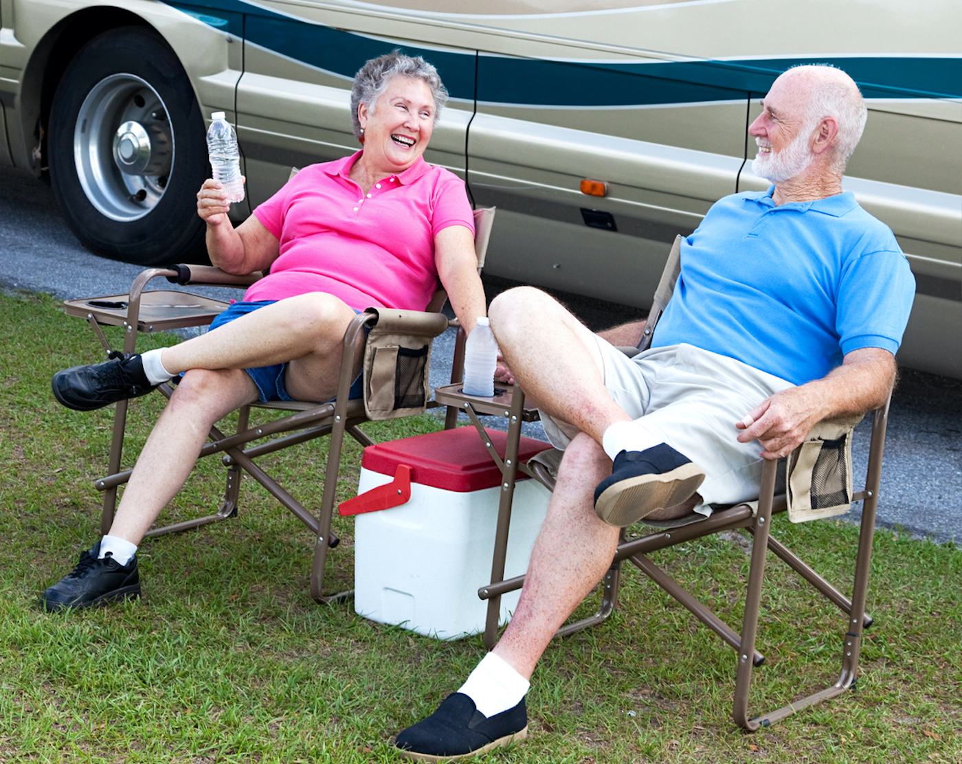 Senior campers sitting holding water bottles in folding chairs outside their motorhome.