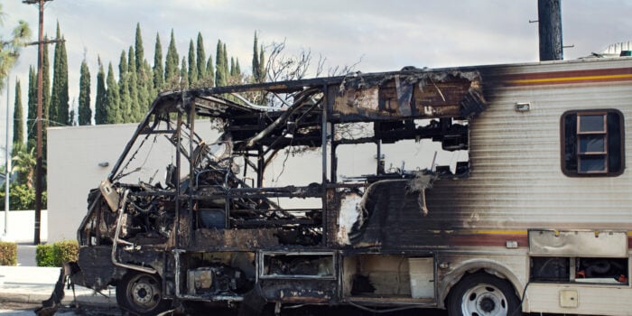burned out rv on pavement with evergreen trees in background
