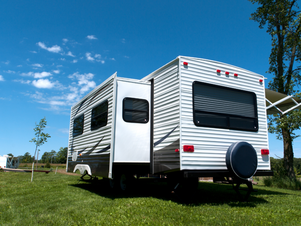 A travel trailer with its pop out extended in a grassy campground.