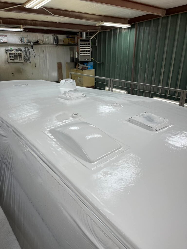 A wide-angle view of a newly finished RV roof inside the FlexArmor Texas shop. The neon lights bounce off the roof highlighting the brilliant white sheen across the roof.