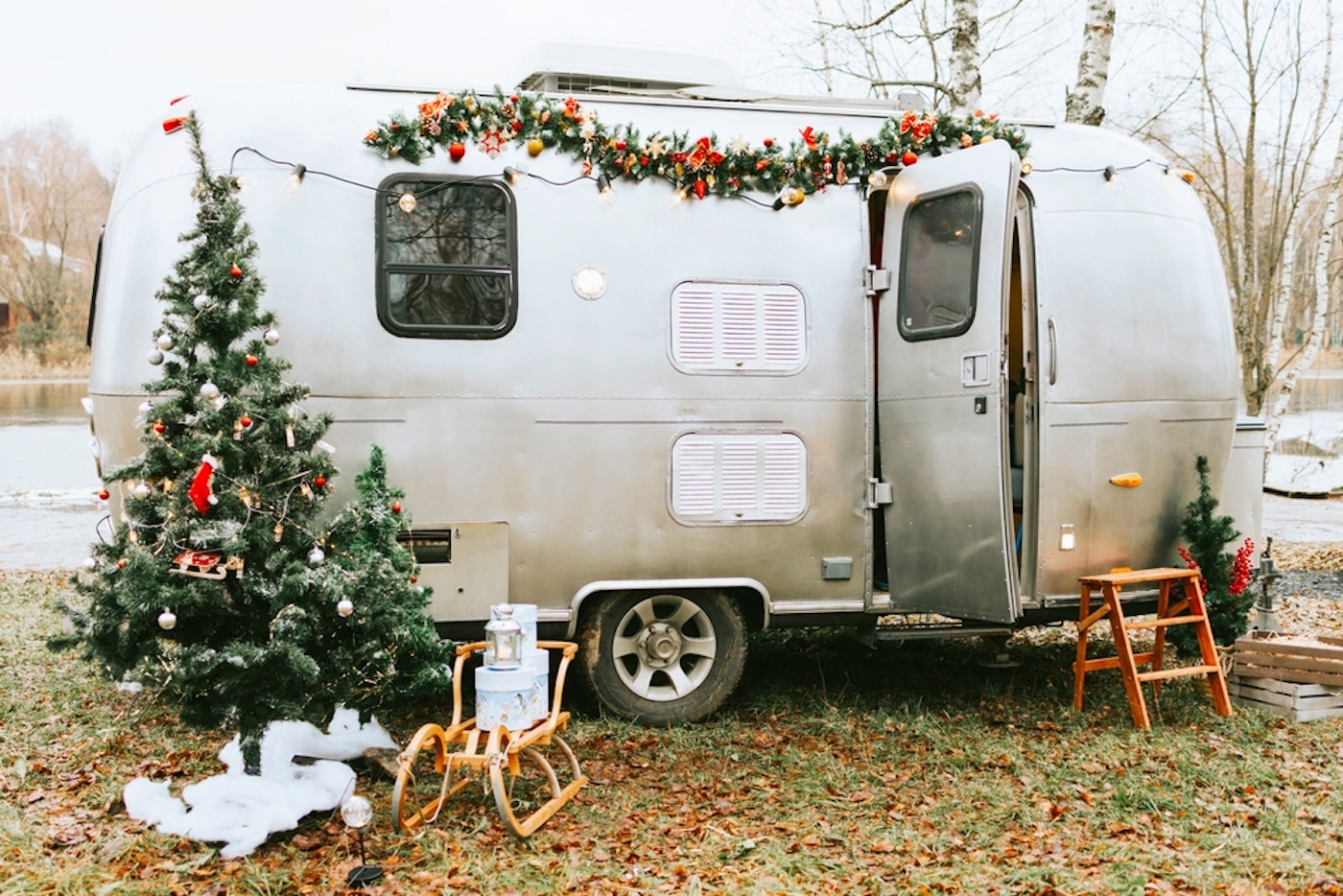 Small Airstream travel trailer decorated for the holidays with a small Christmas tree and sled with evergreen garlands