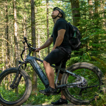 Man sits on electric bike in a wooded trail - Photo: Mokwheel