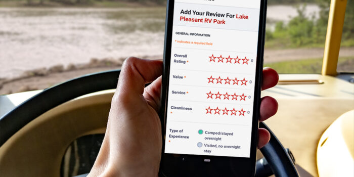 A hand is shown holding a cell phone while using the RV Life app to give a campground review. campground reviews, navigation, RV apps, RV GPS, RV life app, RV Trip Wizard