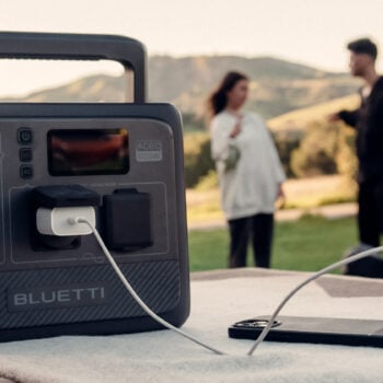 BLUETTI AC60 set on a table with smartphone plugged into it. People chatting and a mountain scenery in the background.