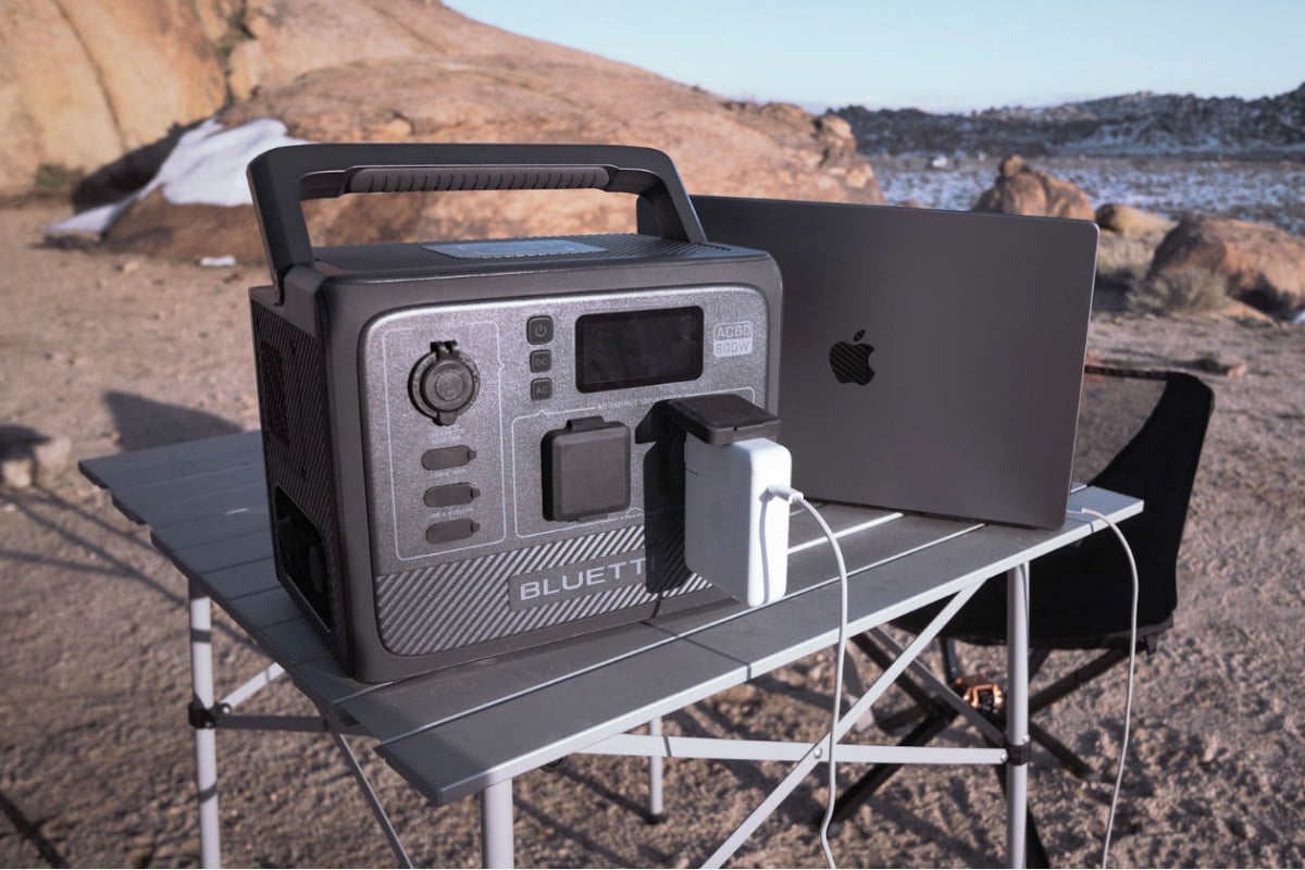 BLUETTI AC60 portable power station set on a table with a laptop plugged in and an ocean setting in the background