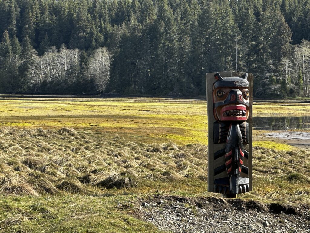 Black bear with fish totem pole on estuary in Port Hardy, BC