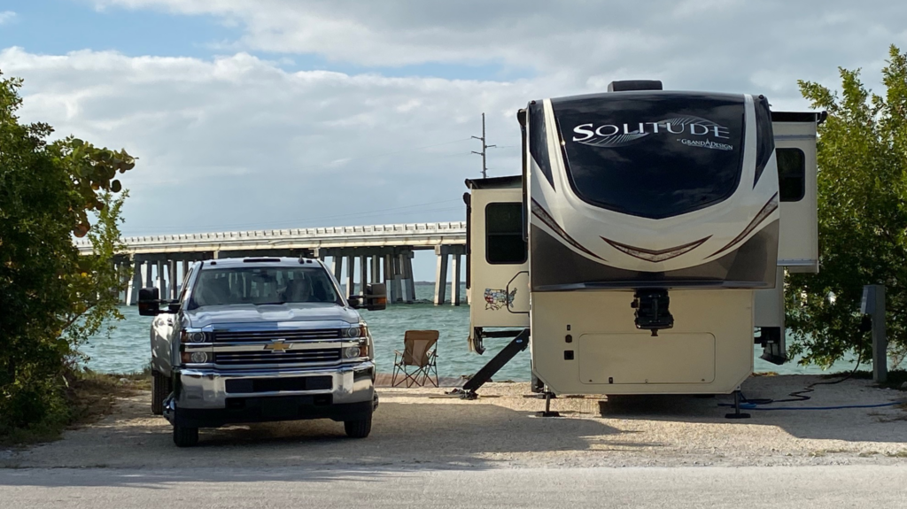 Truck and 5th wheel parked on a big rig friendly coastal campsite with bridge in background.