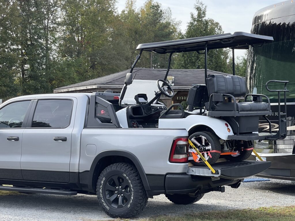 a golf cart being transported in the back of a full-size pickup truck which is then towed behind a motorhome