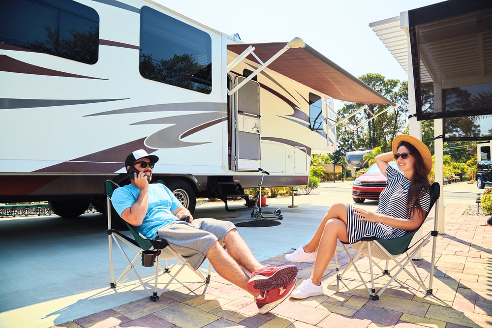 Young man and woman sit outside of a 5th wheel camper.