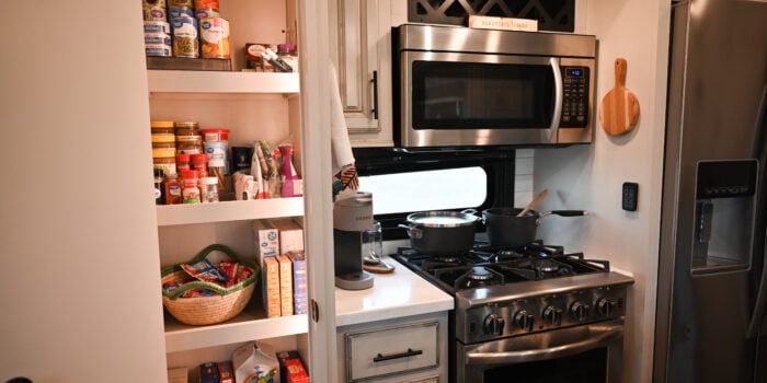 a stainless steel stove top oven sitting inside of a kitchen next to a refrigerator and a refrigerator freezer, image for RV food storage pantry tips