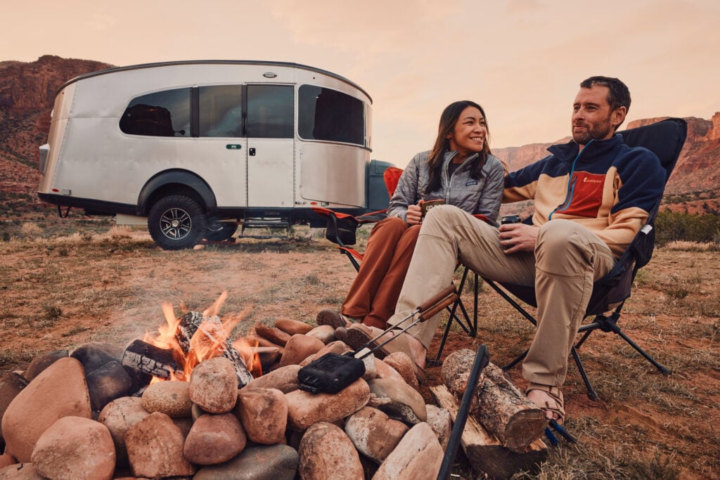 Couple sitting in front of a campfire near Basecamp lightweight travel trailer.
photo: Airstream