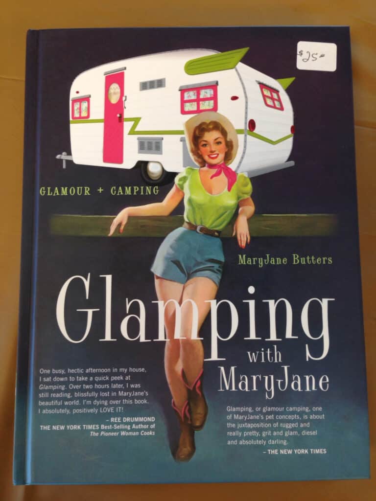 The cover of Glamping With Mary Jane. The words glamour and camping appear, along with a 1950s style woman and retro travel trailer.