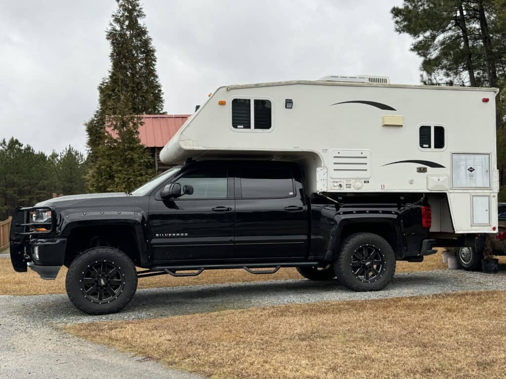 a black truck with a white truck camper fitted over the bed of the truck