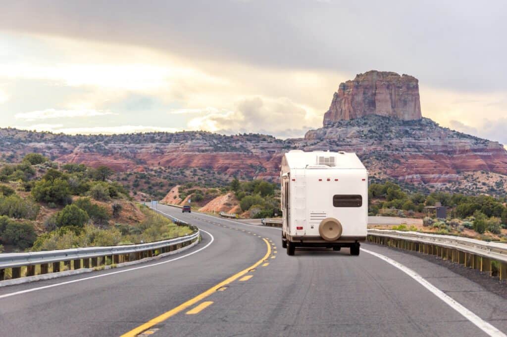 Travel trailer on the highway with rock formations in background.