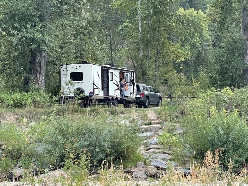 white pickup truck with white travel trailer in heavily wooded campsite