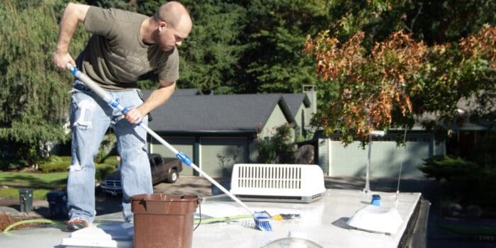 A man on an RV roof cleaning with a scrubber on a pole.