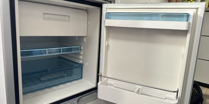 An open RV refrigerator in a kitchen next to a counter with a drawer on one side and a drawer on the other side