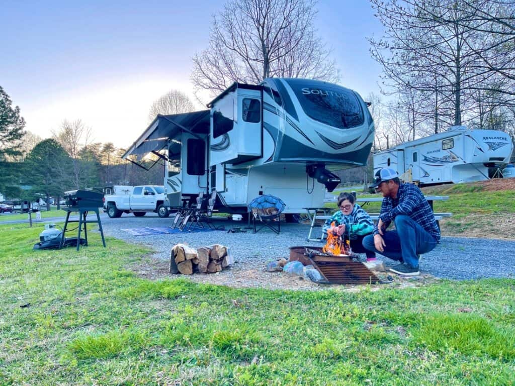 A couple in front of a campfire near their fifth-wheel at a campsite at Honeysuckle Meadows RV Park.
